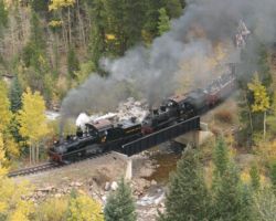 Doubleheaded narrow gauge Shays lumber uphill with a full train of tourists at the plate girder bridge just out of Devil's Gate station.