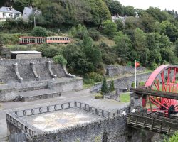 This is the washing floor down in Laxey. Originally the washing floors had a 42' wheel. This is the 50' wheel from the Snaefell mine, which went to Wales in 1908 and came back in 2003. It was restored and installed here in 2006. The old ore chutes are the stone protrusions against the far wall, below the MER train. The 19" mine railway runs on top, and would dump ore down the chutes.