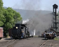 To get 487 out of the shops, the crew needs to move the crane/derrick that's been parked on the engine house lead. Here, they're pushing it to a siding just beyond the coaling tower.