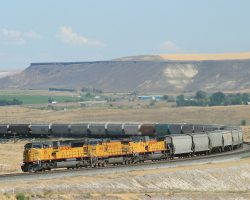 SD90MACs 8510 and 8529 grind uphill west of Hammett, ID, spliced by AC4400W 9684 and towing a long, loaded grain train.